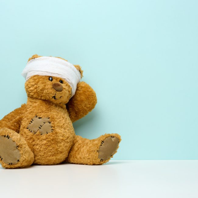 Children's toy teddy bear sits with a bandaged head. Childhood trauma concept