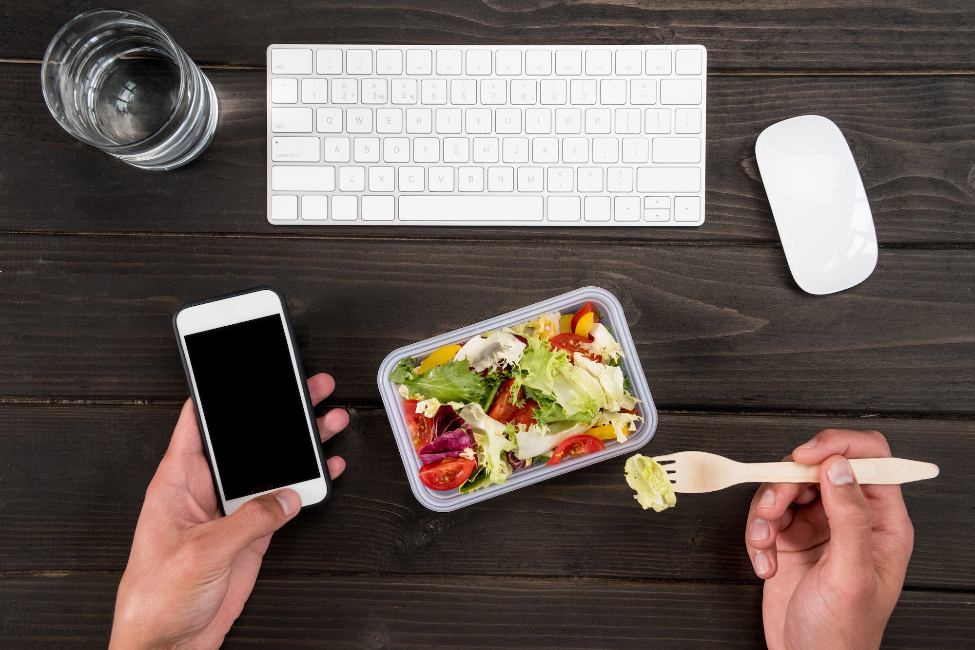 Top view of human hand eating fresh salad and using smartphone during work.