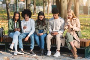 Teenagers sitting on bench in park and using smartphones